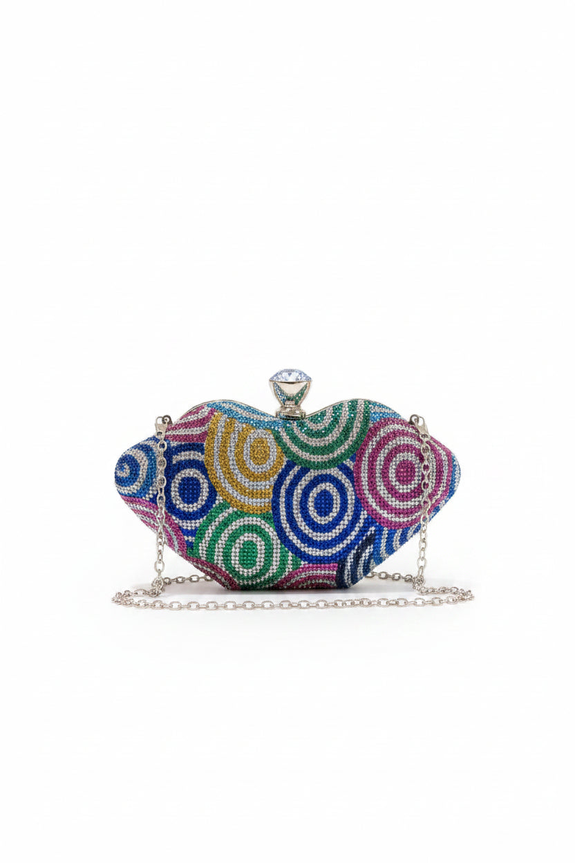 A small heart-shaped evening clutch bag covered in colorful beaded swirl patterns, resting on a white marble table inside a softly blurred boutique.