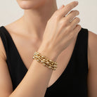 A stack of three gold beaded wrap bracelets with a small white tag attached, resting on a black surface.